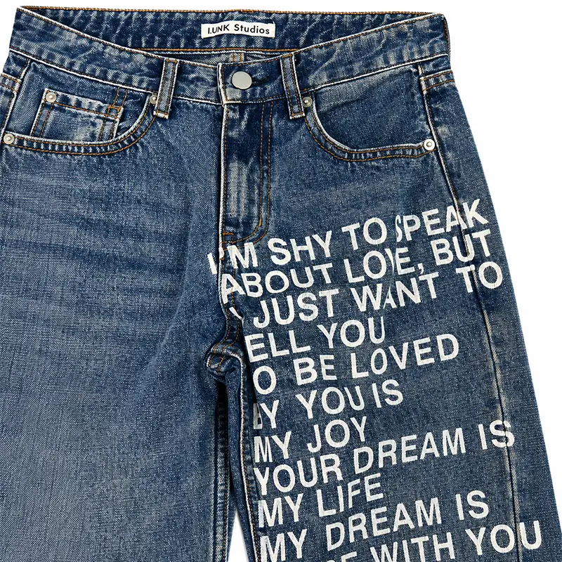 Close-up of custom printed jeans with white text graphic print and medium wash denim