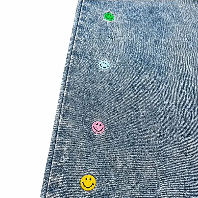 Close-up of custom wide leg jeans with colorful smile buttons on light wash denim fabric
